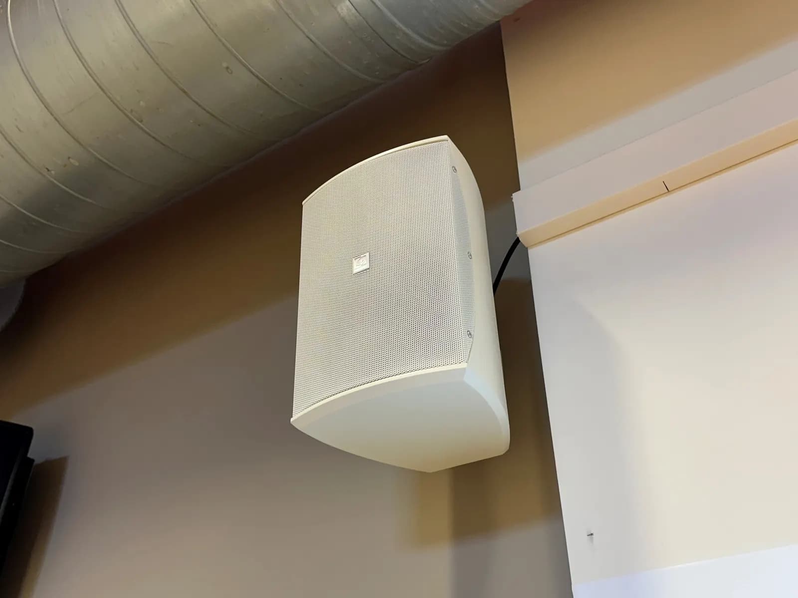Enceinte blanche fixée au mur de la petite salle.