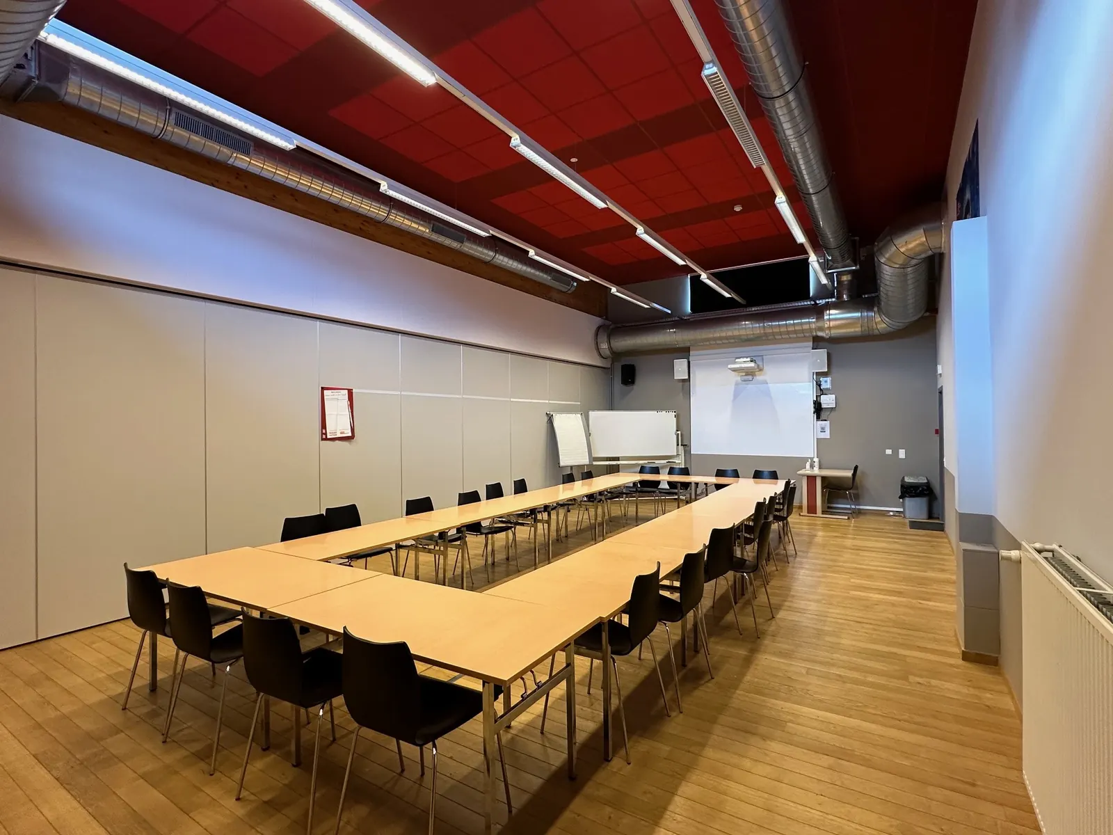 Petite salle vue depuis l'entrée : tables en U, plafond rouge et écran de projection au fond.